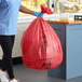 A woman in blue scrubs holding a red medical waste bag.