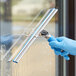 A person wearing blue gloves using a Lavex window squeegee to clean a window.