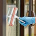 A hand in a blue glove using a Lavex 10" window squeegee to clean a window.