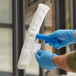 A person in blue gloves using a Lavex white fabric strip washer on a window.
