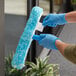 A person wearing blue gloves using a Lavex 14" T-Bar Handle to clean a window.