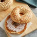 Two Original Bagels, one with cream cheese and one with oats on a cutting board.