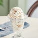 A glass cup with a scoop of ice cream topped with chopped REESE'S Peanut Butter Cup.