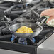 A person using a Vollrath Wear-Ever aluminum non-stick fry pan to cook eggs on a stove.