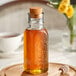 A close up of a 12 oz. glass Muth honey jar with a cork on a wooden tray.