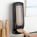 A person putting a brown paper bag into a black Tork Xpressnap standing wall mount dispenser.