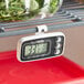 A digital refrigerator and freezer thermometer with a display and control buttons, hanging from a metal shelf.