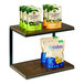 A Cal-Mil dark oak 2-tier shelf display with bags of snacks on the shelves.