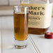 An Arcoroc cordial glass filled with brown liquid next to a bottle of liquor.