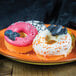 A plate of Silikomart mini donuts with white frosting and Halloween decorations, including a pink donut with a skull and sprinkles, and a donut with white frosting and black candy on top.