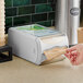 A person using a Tork gray countertop napkin dispenser.