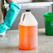 A gloved hand holding a translucent HDPE jug of orange liquid.
