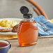 A Classic Queenline PET bottle of honey with a black plastic flip top lid on a table with food.