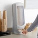 A person standing next to a Tork Xpressnap napkin dispenser holding a napkin.