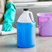 A translucent HDPE jug with black cap filled with blue liquid next to a bucket.