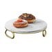 A Cal-Mil white marble display riser with gold accents holding a plate of donuts.