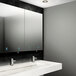 A white bathroom with a stainless steel cabinet with mirror, paper towel, and soap dispensers above a white sink.