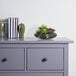 A black dish planter with artificial succulents on a dresser.