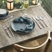 An Acopa Phoenix stainless steel dinner spoon on a table with silverware and a glass.