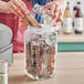 A person's hand filling a clear glass jar with food.