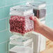 A hand holding a clear Acopa square glass jar of chocolate chips.