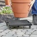 A person using a black Regency solid-surface dolly to move a large pot.