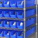 A metal shelf with Regency blue bins holding white containers.