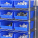 A metal shelving unit with blue Regency shelf bins holding white plastic fittings.