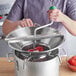 A woman using a Garde rotary food mill to press tomatoes in a large pot.