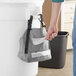 A person holding a Lavex Gray Double Pocket Trash Bag in front of a trash can.