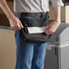 A man using a black Lavex waist trash bag dispenser to hold a bag at a trash can.