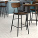 A Lancaster Table & Seating black barstool with wood seat and backrest on a table next to a counter.