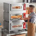 A man putting pizza into a triple deck countertop oven.