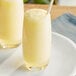 Two glasses of yellow smoothies with straws on a white plate.