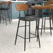 A Lancaster Table & Seating black barstool with a wood back and black vinyl seat.