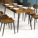 A Lancaster Table & Seating butcher block table with plates and glasses on it and chairs with wood seats and black legs.