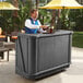 A man standing behind a Cambro portable bar serving a drink.