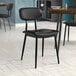 A Lancaster Table & Seating black chair with black vinyl padded seat and backrest on a table in a restaurant dining area.