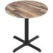 A round wooden table with a black cross base.