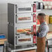 A man in an apron putting pizza into an Avantco quadruple deck countertop oven.