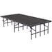 A National Public Seating portable stage with a gray carpeted top set up on a black rectangular table.