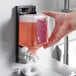 A hand holding a SC Johnson Professional Rose Foaming Hand Soap bottle with pink liquid.