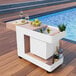 A white Astella mobile bar with food and drinks on it by a pool.