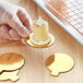 A hand holding a small cake on a gold dessert board with a tab.