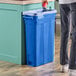 A man in a pair of jeans standing next to a Lavex Pro blue slim rectangular trash can.