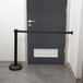 A black Aarco wall mounted stanchion barrier on a door.