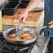 A person cooking food in a Vollrath stainless steel fry pan on a stove.