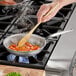 A person stirring food in a Vollrath aluminum fry pan on a stove.