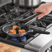 A hand using a Vollrath stainless steel frying pan with a black silicone handle to cook scallops.