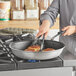 A person cooking meat in a Vollrath Wear-Ever non-stick fry pan.